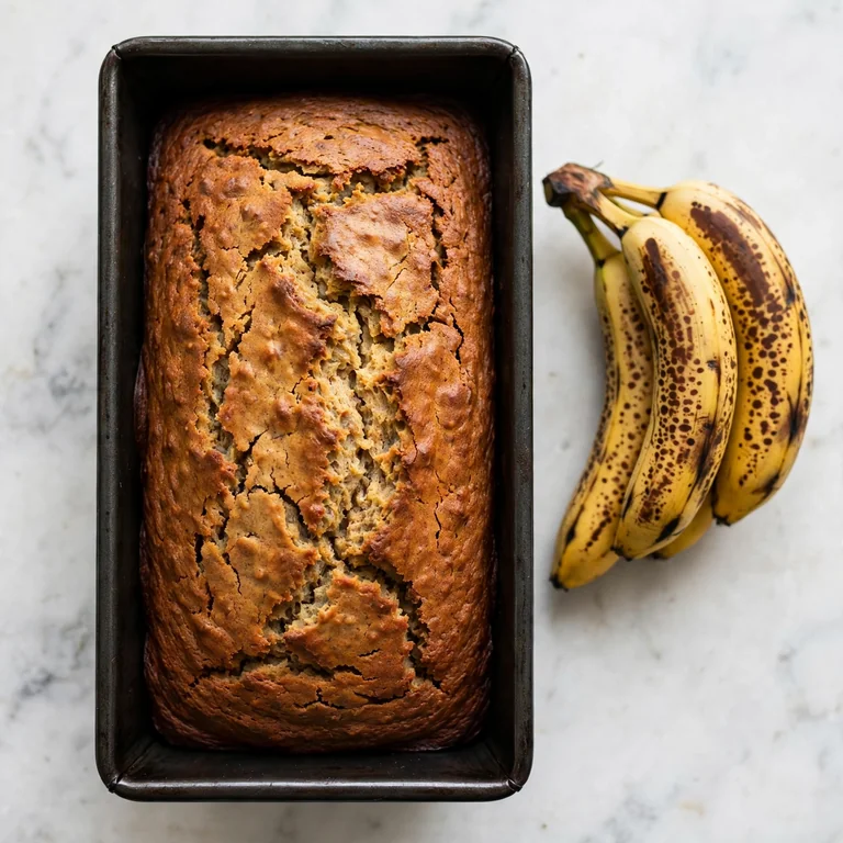 Whole banana bread loaf in dark pan with overripe bananas on marble surface