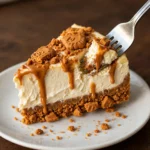 Fork cutting a bite from Biscoff cheesecake slice in white plate