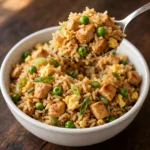 Spoon lifting chicken fried rice with egg and green onion from a white bowl