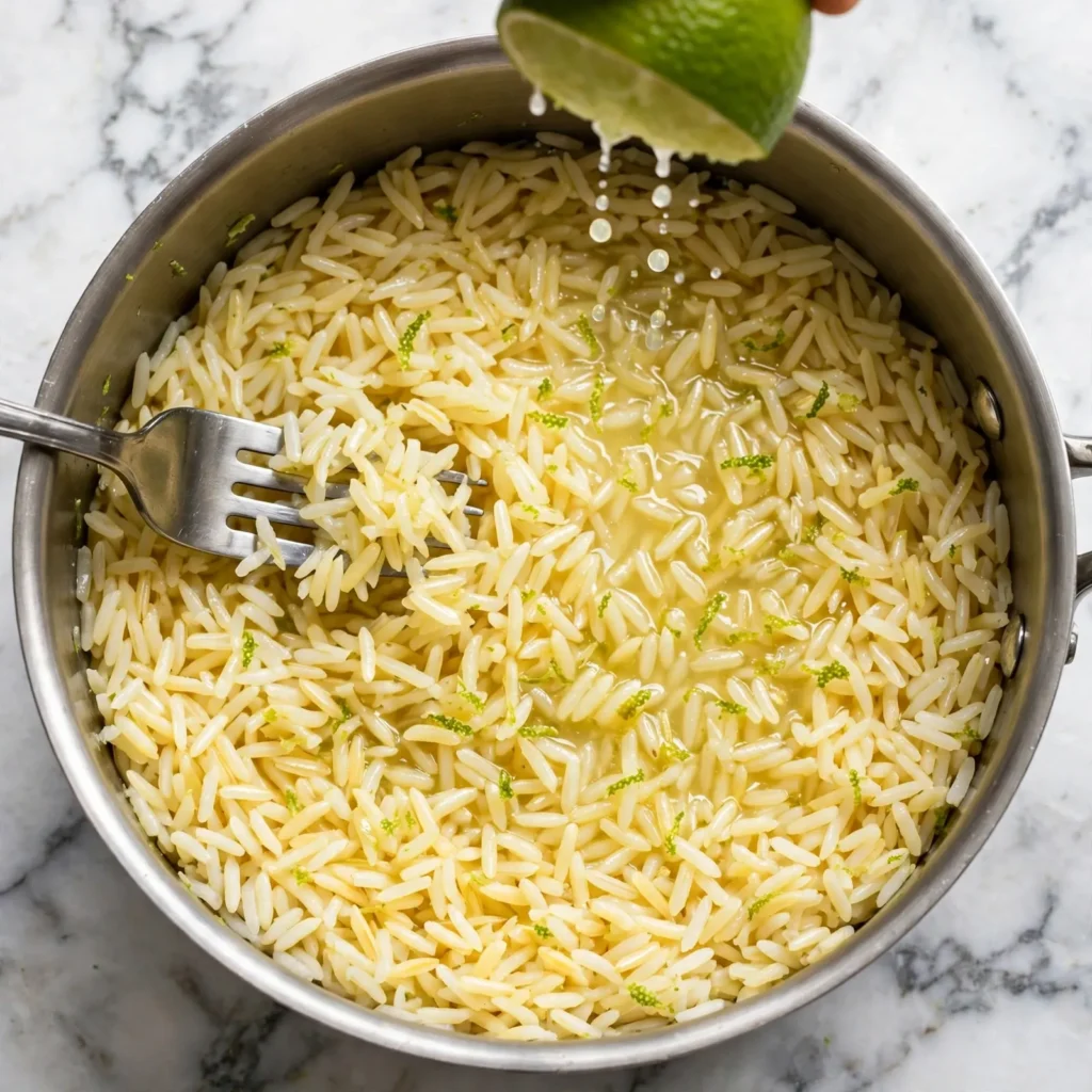 Cooked fluffy rice being fluffed with a fork as lime juice is drizzled over it off the heat