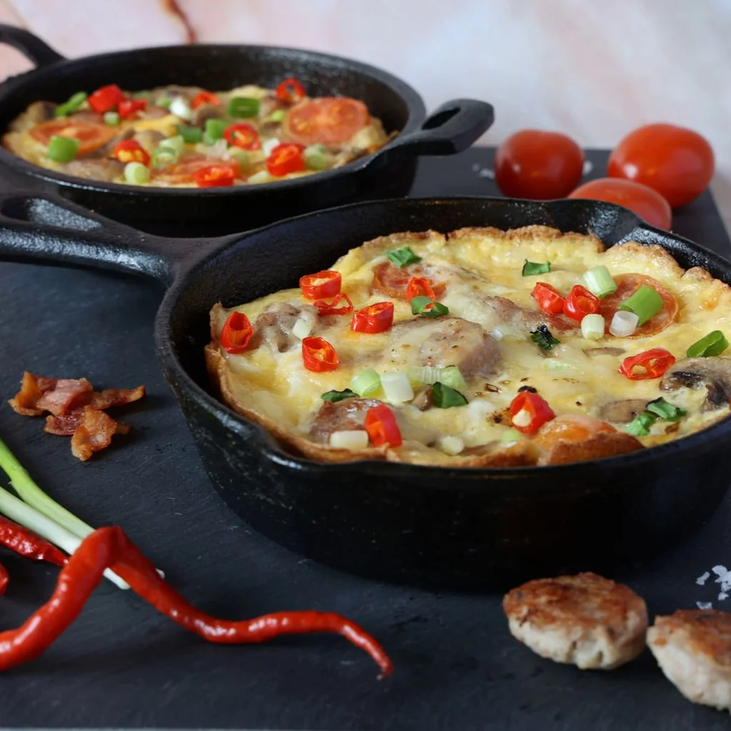 Six golden egg muffins in a white ceramic muffin tin, each filled with visible spinach, red bell pepper, and melted cheese peeking through the tops. Slightly domed and golden brown on the surface. Warm kitchen light from above. Top-down food photography on a gray linen surface.